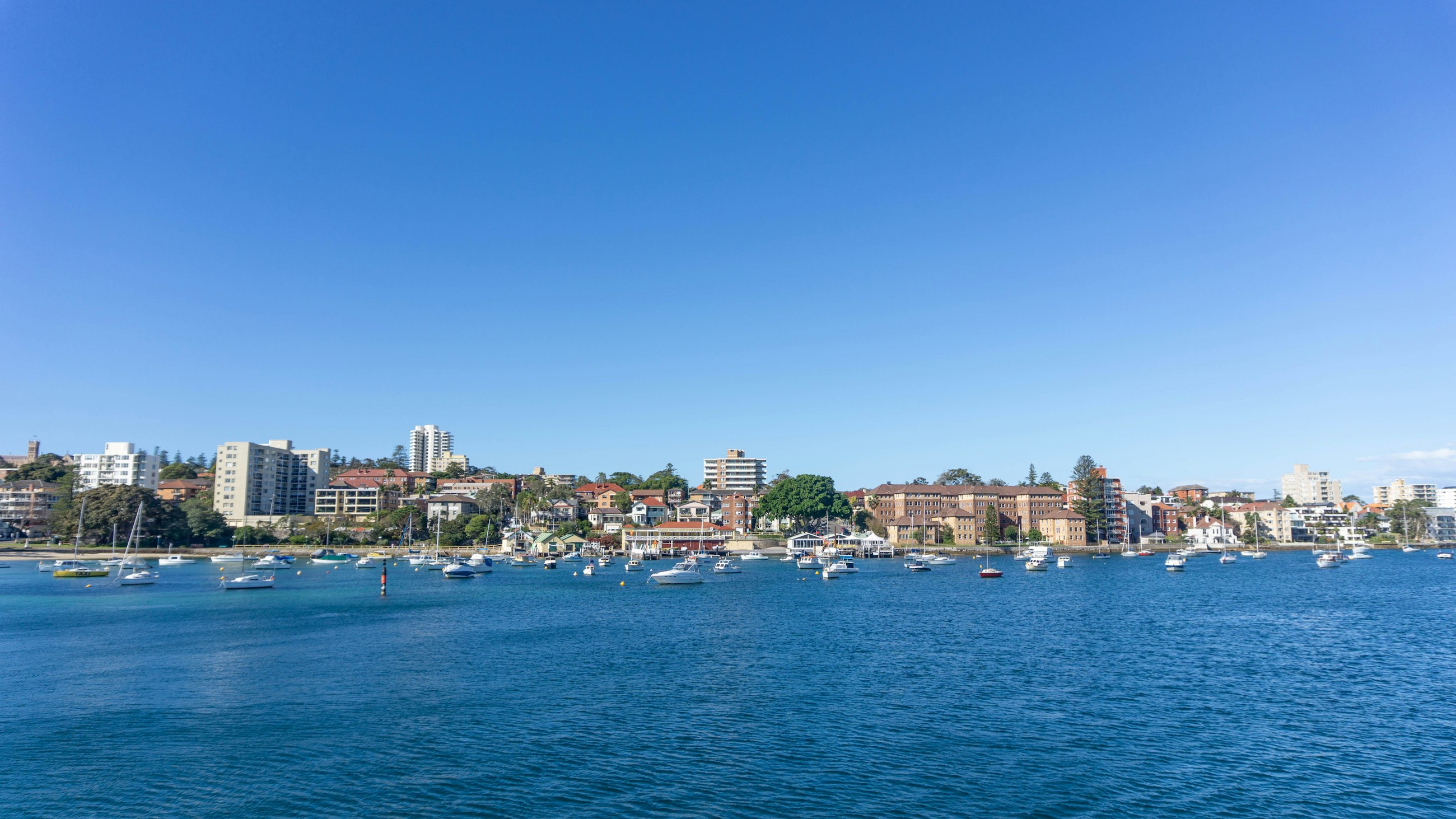 Manly's waterfront and the boats moored in Manly Cove, seen from the harbour on a clear day.