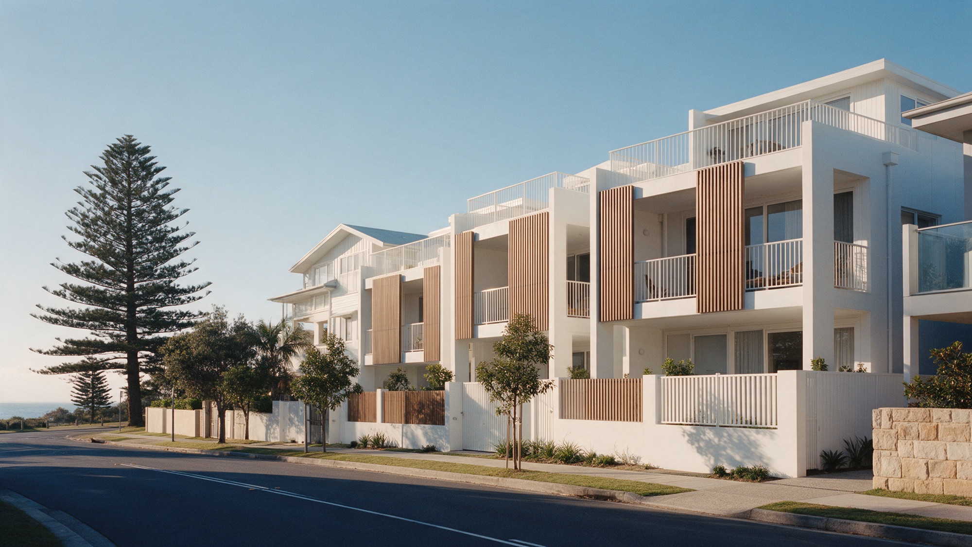 Modern coastal townhouses with timber screens on a tree-lined street.
